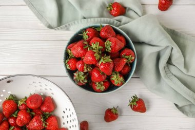 Beyaz ahşap arka planda taze çilekli kevgir ve kevgir