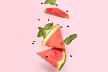Uçan taze karpuz parçaları ve pembe arka planda nane ve tohumlar.