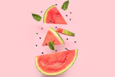 Uçan taze karpuz parçaları ve pembe arka planda nane ve tohumlar.