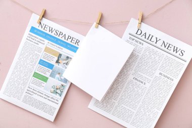 Gazeteler ve boş kağıtlar pembe arka planda ipte sallanıyor.