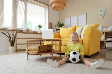 Evde yerde oturan futbol topuyla tatlı küçük bir kız.