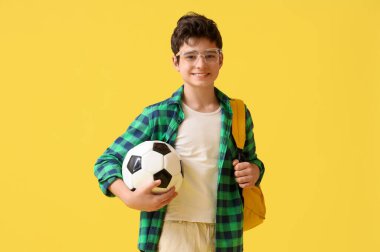 Sarı arka planda futbol topu olan genç bir çocuk.