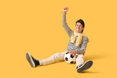 Futbol topuyla genç çocuk sarı arka planda başarıyı kutluyor.