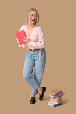 Kahverengi arka planda bir sürü kitabı olan güzel, mutlu bir kadın.