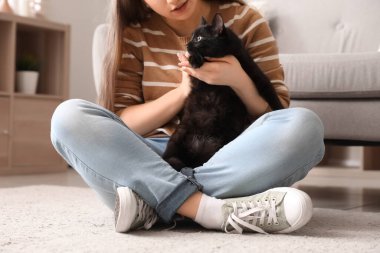 Oturma odasında oturan sevimli siyah kedili kadın.