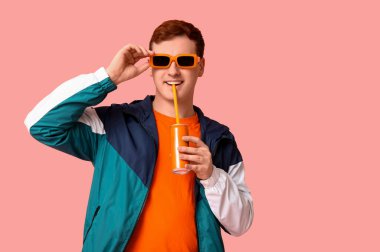 Güneş gözlüklü genç adam pembe arka planda soda içiyor.