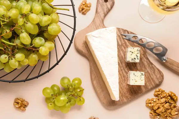 Lezzetli peynirli ahşap tahta, bej arka planda üzüm ve fındık.