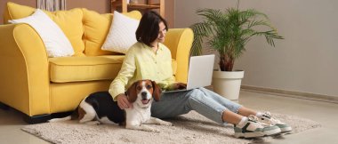 Evde yerde dizüstü bilgisayar kullanan Beagle köpeği olan genç bir kadın.