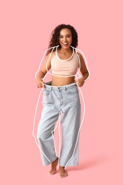 Pembe arka planda kilo verdikten sonra bol elbiseli mutlu genç kadın.