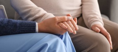 Evde el ele tutuşan yaşlı bir kadınla genç bakıcı, yakın çekim.