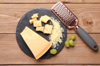 Slate board with pieces of tasty Parmesan cheese on wooden background clipart