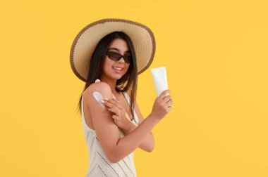 Sarı arka planda güneş kremi süren güzel genç bir kadın.