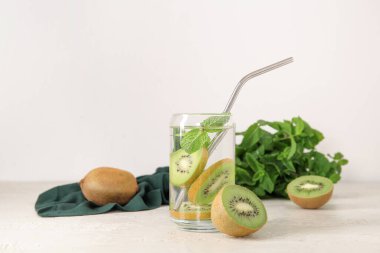 Beyaz zemin üzerinde kivi ve nane ile doldurulmuş su bardağı