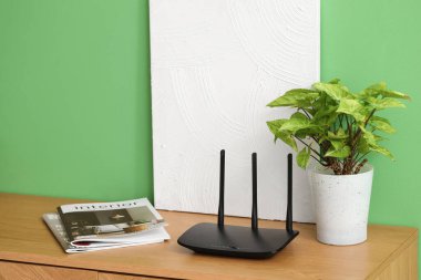 Yeşil duvarın yanındaki rafta bitki, dergi ve boya ile modern wi-fi yönlendirici