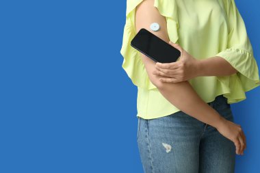 Kan şekeri seviyesini ölçmek için glikoz sensörü olan bir kadın ve mavi arka planda telefon. Diyabet kavramı