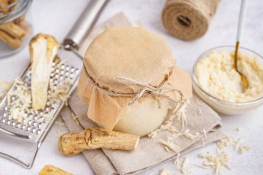 Beyaz arka planda yabanturpu kökleri olan yabanturpu sosu kavanozu.