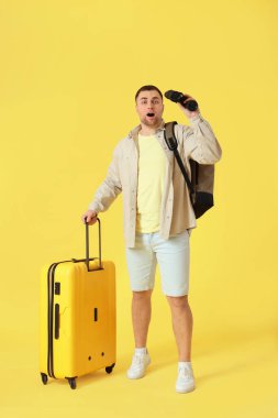 Sarı arka planda bavulu ve dürbünü olan erkek turist.