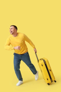 Sarı arka planda bavulla koşan erkek turist.