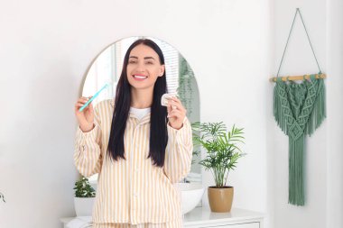 Evdeki banyoda diş ipi ve diş fırçasıyla güzel, genç, mutlu bir kadın.