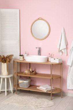 Banyodaki pembe duvarın yanındaki raflarda banyo malzemeleri olan modern lavabo.