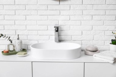Banyodaki beyaz tuğla duvarın yanında banyo malzemeleri olan modern lavabo.