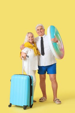 Yüzme yüzüğü ve bavulu olan olgun iş adamları sarı arka planda yaz tatiline hazır.