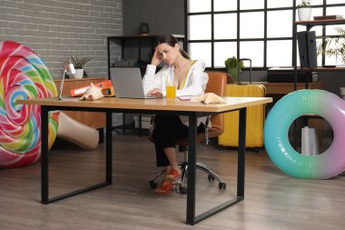 Ofiste dizüstü bilgisayarla oturan hayal kırıklığına uğramış kadın ofis çalışanı. Yaz tatili kavramı