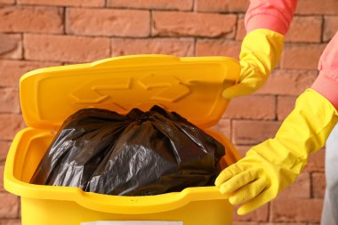 Tuğla duvarın yanındaki çöp kutusundan çöp torbası alan kadın.