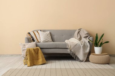 Oturma odasındaki bej duvarın yanında ekose ve çiçekli gri rahat kanepe.