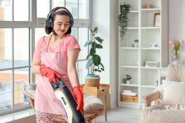 Elektrikli süpürgeyle oturma odasında müzik dinleyen genç bir kadın.