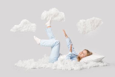 Adorable girl with white clouds lying on grey background clipart