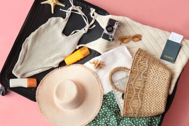Şık kadın kıyafetleri, plaj aksesuarları, pasaport ve fotoğraf makinesi olan bavul.