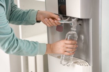 Kadın elleri plastik şişeyi soğutucudan filtrelenmiş suyla dolduruyor.