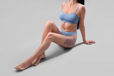 Açık mavi iç çamaşırlı güzel bir kadın beyaz arka planda oturuyor.