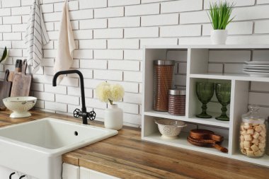 Mutfak tezgahları lavabo, raflar ve çatal bıçaklar beyaz tuğla duvarın yanında.