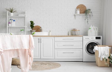 Çamaşır makinesi, sepeti ve tezgahı olan çamaşır odasının içi.