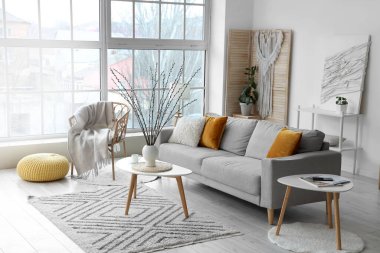 Oturma odasının içinde kanepe, koltuk ve vazoda söğüt dalları var.