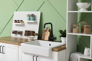 Mutfakta yeşil duvarın yanında tahta, lavabo ve çiçek var.