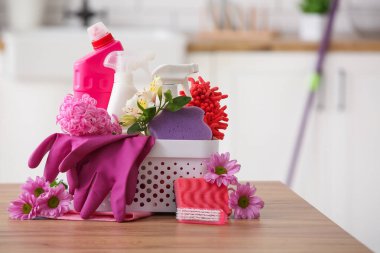 İçinde temizlik malzemeleri ve bahar çiçekleri olan sepet mutfaktaki ahşap masada.