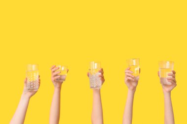 Sarı arka planda farklı su bardakları olan kadın eller.