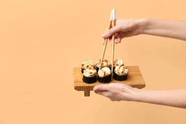 Hands with tasty maki rolls and chopsticks on beige background