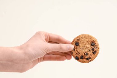 Female hand holding sweet cookie with chocolate chips on white background