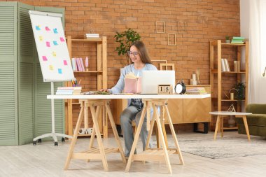 Female tutor with book and calculator giving online Math lesson at home