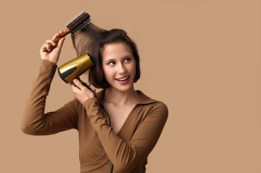 Güzel, genç, mutlu bir kadın. Saç kurutma makinesi ve kahverengi arka planda fırçası var.