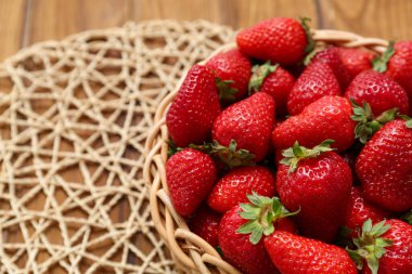 Ahşap zemin üzerinde taze çilekler olan hasır bir kase.