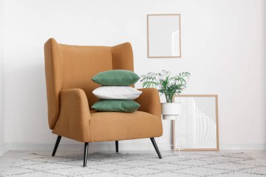 Beyaz duvarın yanında yastık yığını olan rahat bir koltuk.