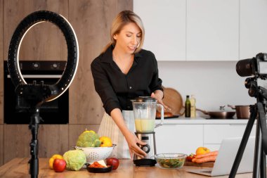 Kadın yemek blogcusu mutfakta video kaydederken sebze smoothie yapıyor