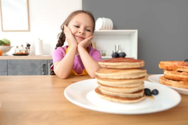 Sevimli küçük kız ve mutfaktaki masada ballı krep, yakın plan.
