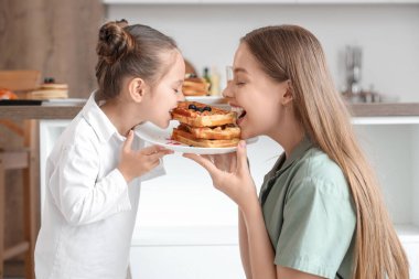 Sevimli küçük kız ve annesi mutfakta ballı waffle yiyorlar.