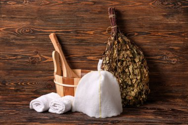 Keçeli şapka, temiz havlular, kova ve ağaç süpürgesi ahşap arka planda sauna için.